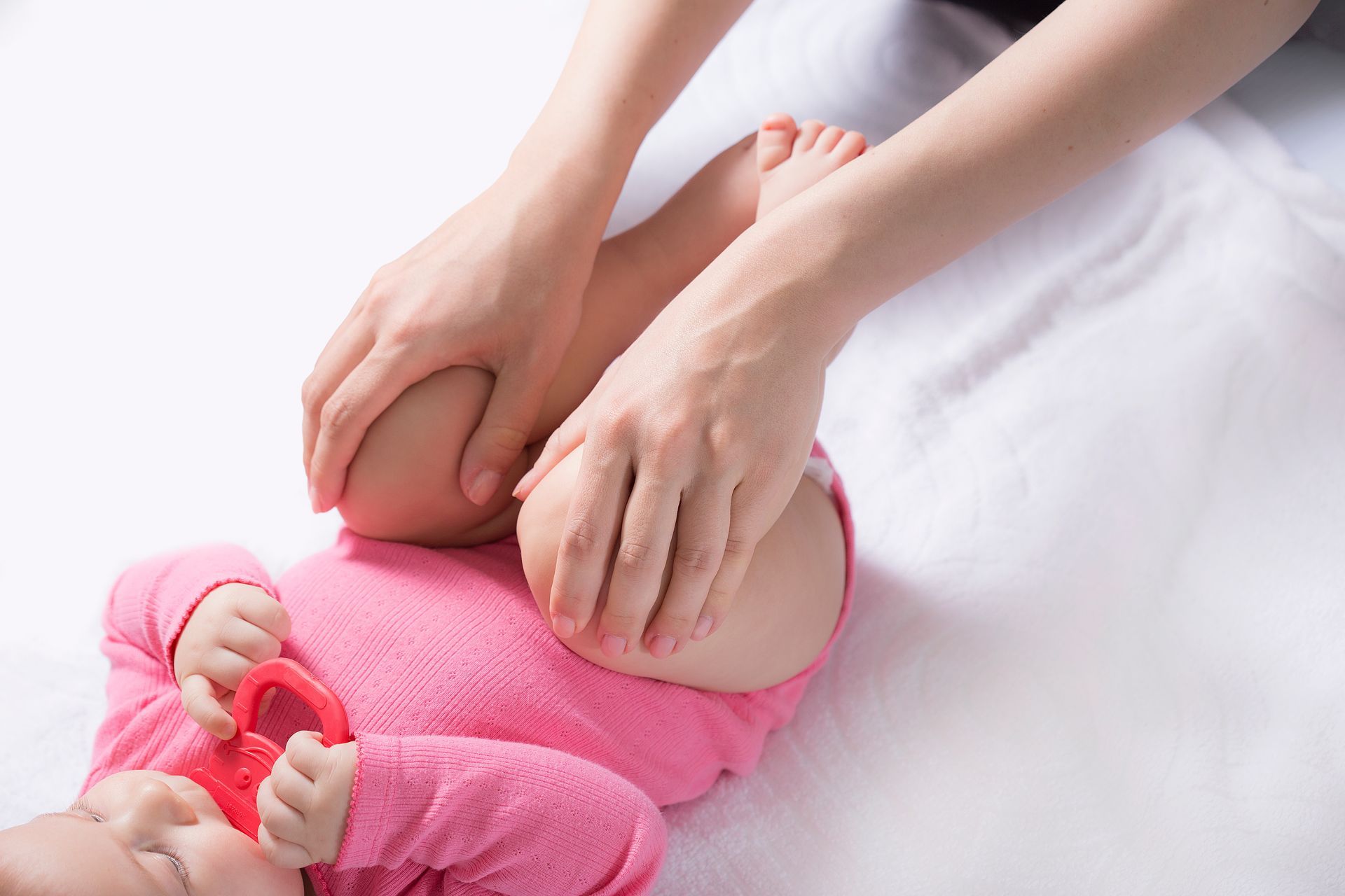 Hände massieren die Füße eines Babys auf einer weißen Decke; das Baby trägt rosa Kleidung.