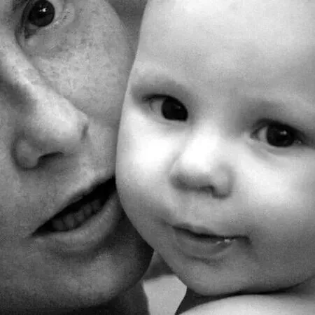 Nahaufnahme in Schwarz-Weiß: Ein Erwachsener und ein lächelndes Baby, Wange an Wange.