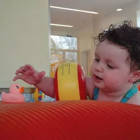 Ein Baby greift in einem hellen Spielzimmer nach einem Spielzeug über einem roten Kissen.