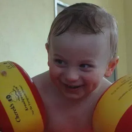 Lächelndes Kind mit gelben Schwimmflügeln am Pool oder in der Badewanne