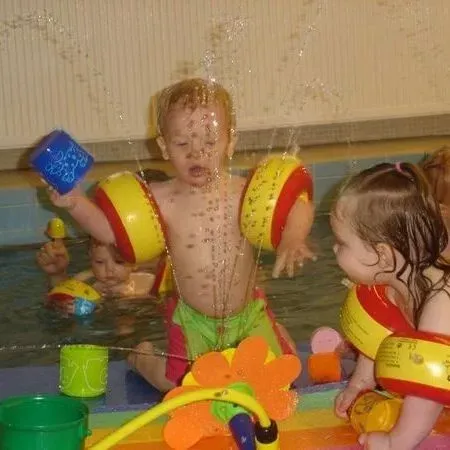 Kinder spielen mit bunten Schwimmreifen in einem Hallenbad unter einem Wassersprüher