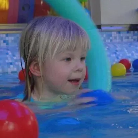 Kind in einem Schwimmbecken mit einem roten Ball und bunten schwimmenden Spielzeugen, lächelnd nahe der Wasseroberfläche