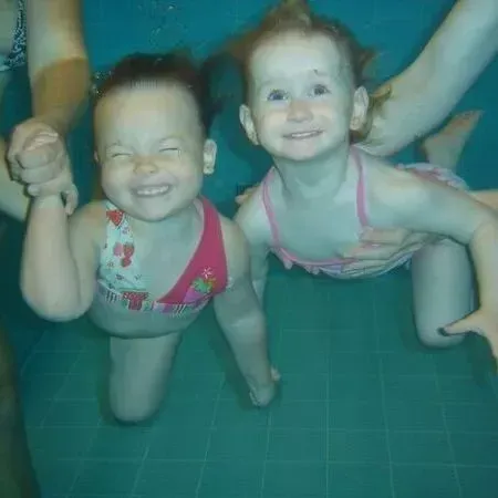 Zwei lächelnde Kinder unter Wasser in einem Pool, die Hände haltend und die Arme erhoben
