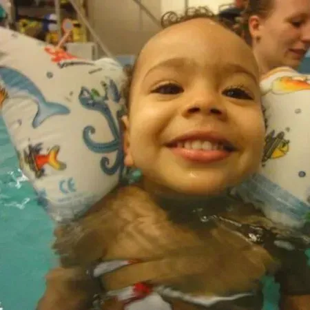 Ein lächelndes Kind mit bunten Schwimmflügeln in einem Schwimmbecken, nah an der Kamera