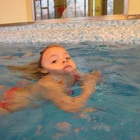 Kind schwimmt in einem Hallenbad, das Gesicht über Wasser nahe einer gefliesten Wand