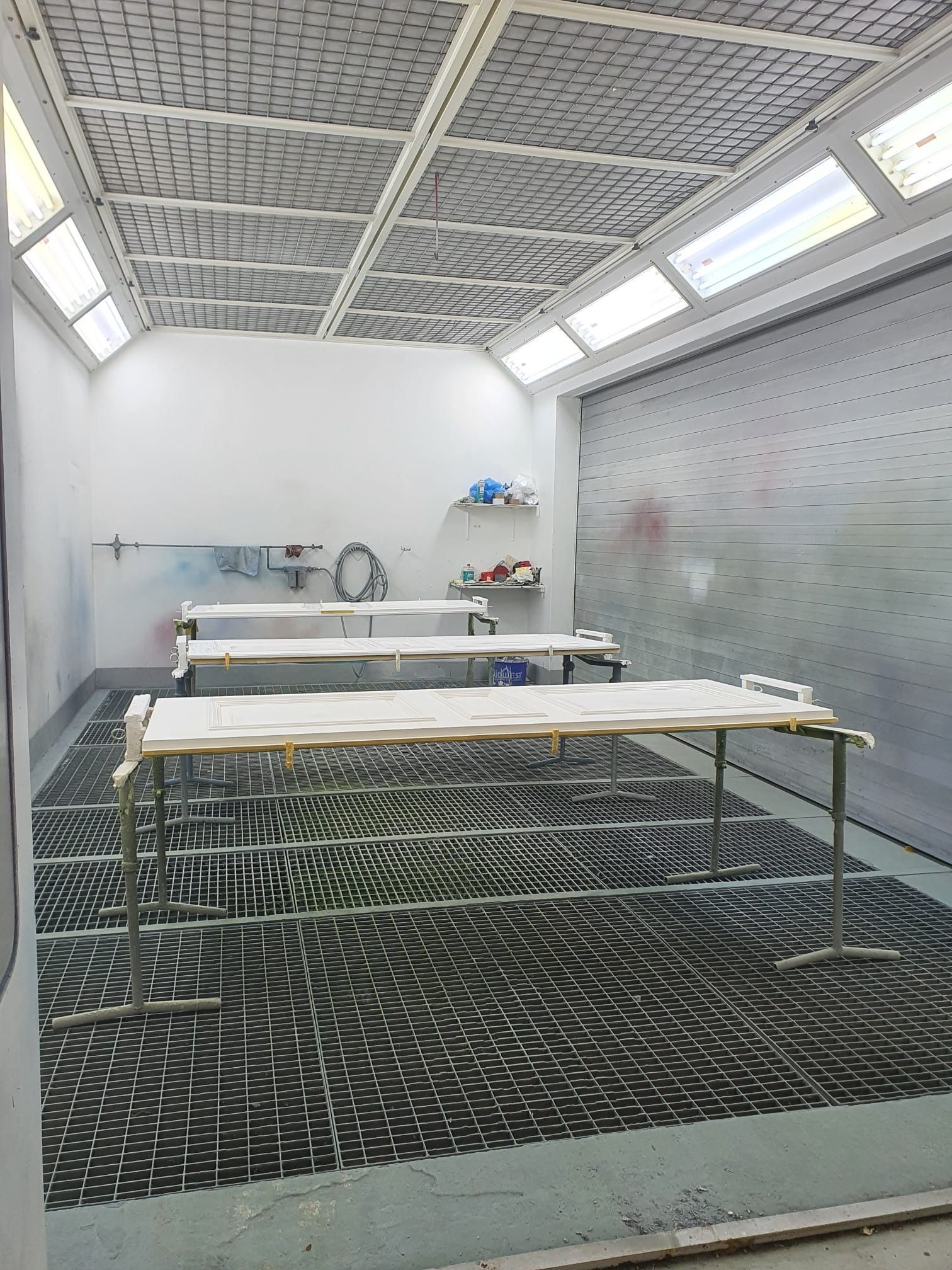 Kleine, industrielle Werkstatt mit zwei Tischen, an der Wand montierten Werkzeugen und einem gemusterten schwarzen Boden.