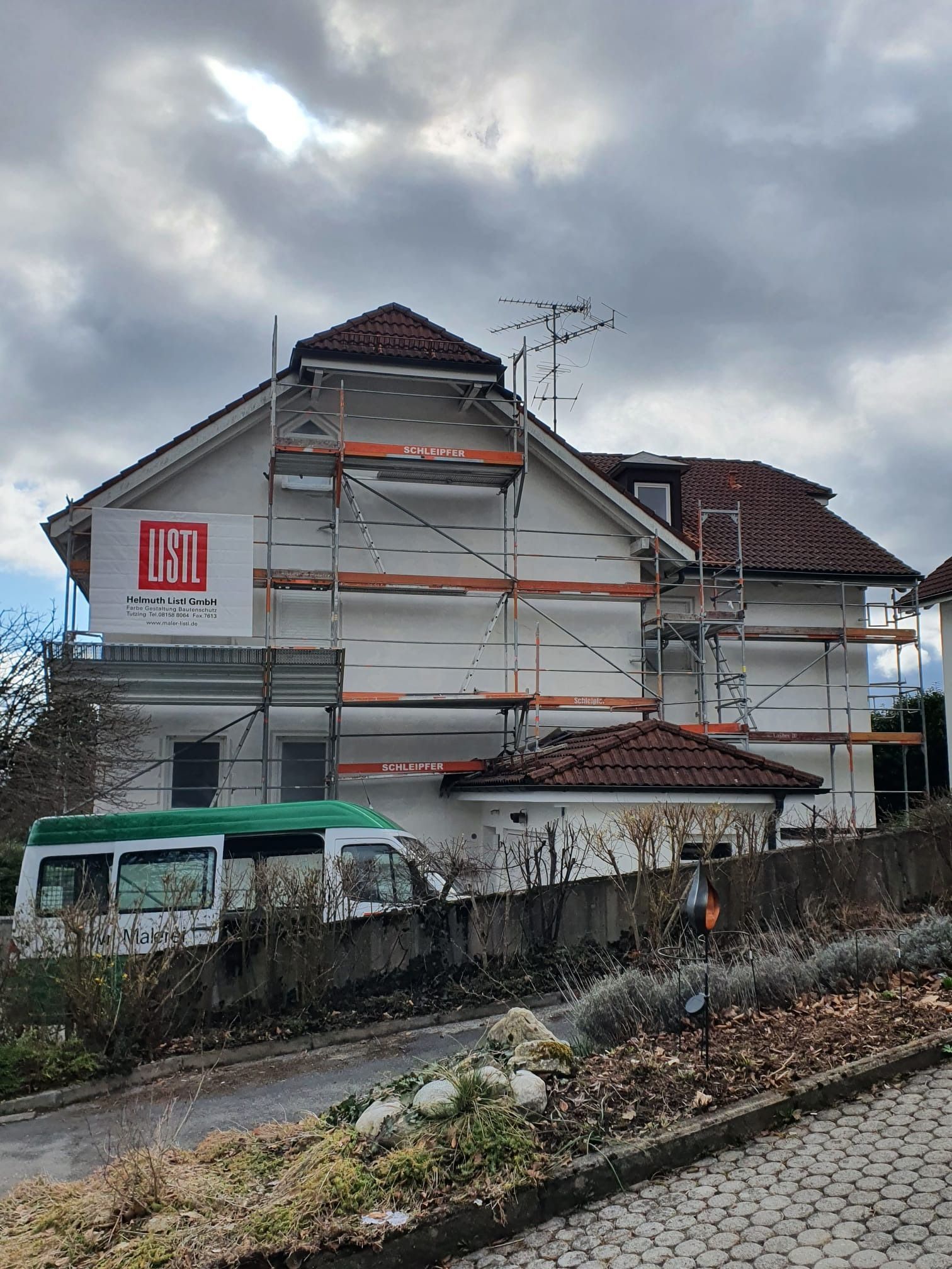 Haus im Umbau mit Gerüst und weißer Schutzplane neben einem geparkten Lieferwagen