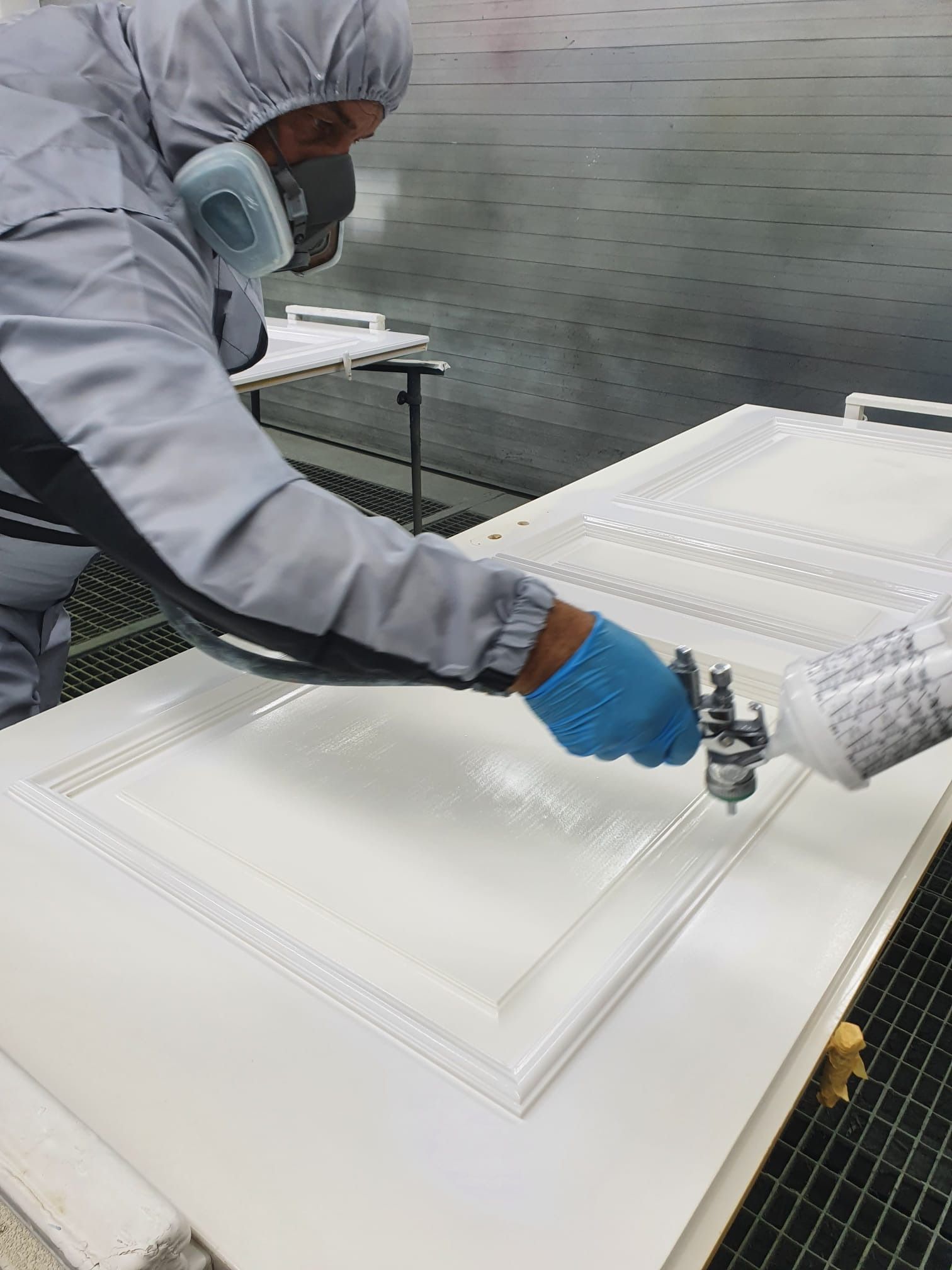Ein Arbeiter in Schutzkleidung besprüht weiße Paneele in einer sauberen Industriehalle.
