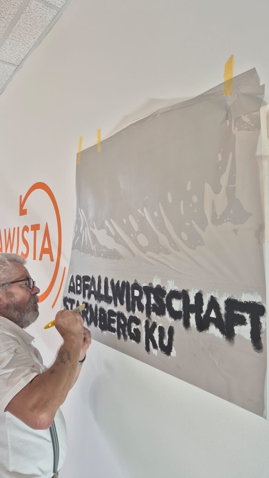Ein Mann in weißem Hemd klebt eine große, durchsichtige Folie über einen schwarzen Text an einer Wand.