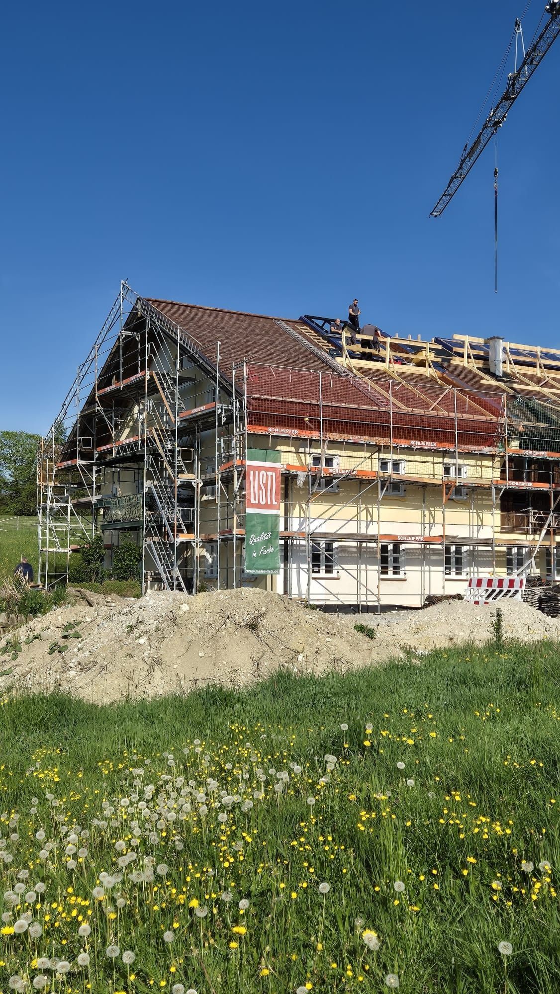 Haus im Umbau mit Gerüst an einem sonnigen Tag, neben einer Wiese und klarem blauen Himmel