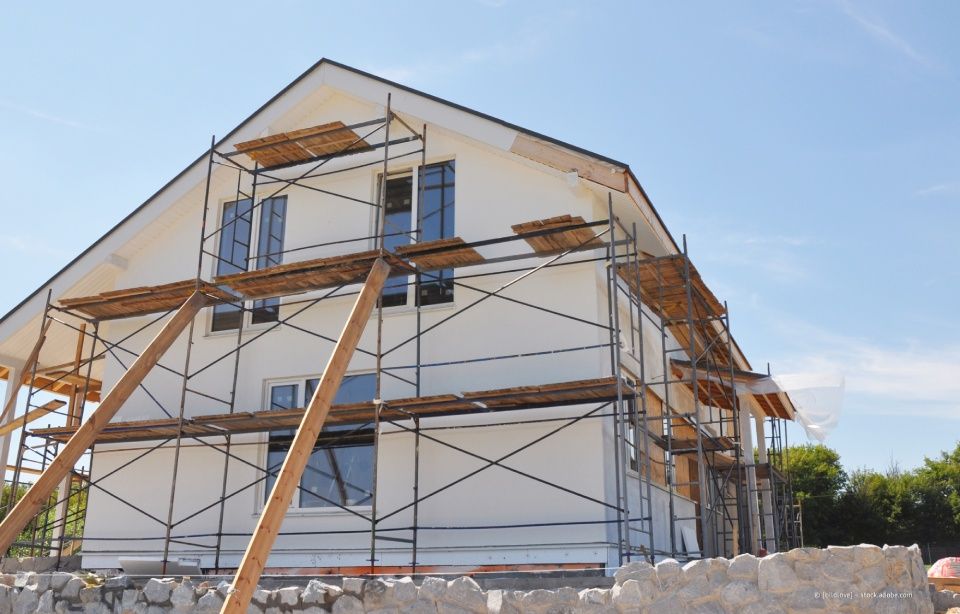 Haus im Bau mit Gerüst und Holzstützen unter blauem Himmel