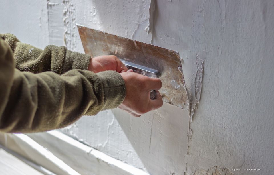 Eine Person trägt bei Reparaturarbeiten mit einer Kelle Gips auf eine weiße Wand auf.