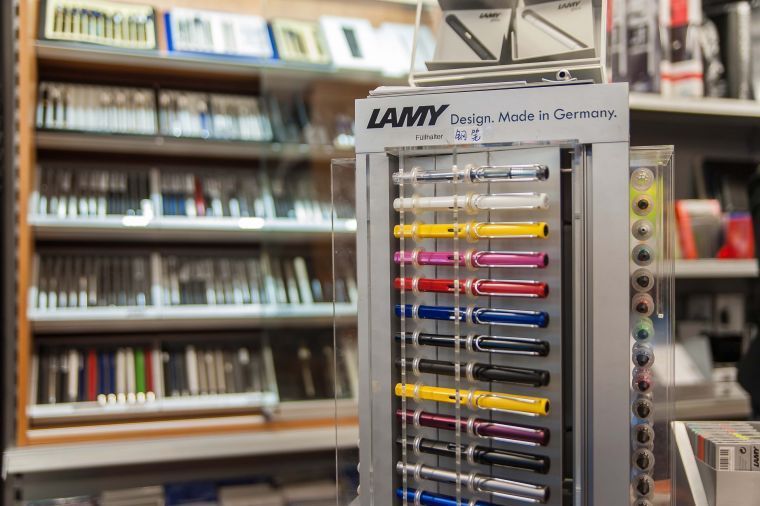 Ein LAMY-Stifteständer mit bunten Stiften in einem Schreibwarengeschäft, im Hintergrund verschwommene Regale.