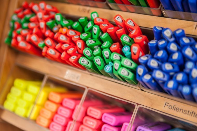 Bunte Filzstifte und Kugelschreiber in Behältern, mit roten, grünen, blauen, gelben und pinkfarbenen Kappen.