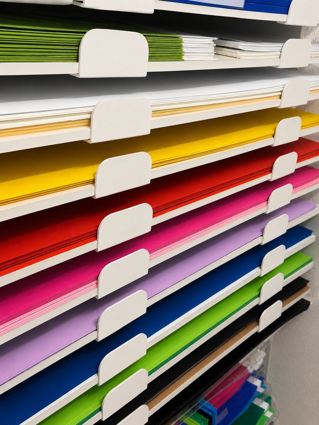 Regale voller buntem Papier in weißen Haltern, nach Farben sortiert, in einem Ladengang.