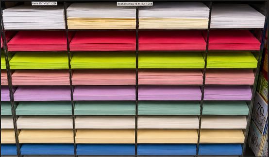 Gestapelte Regale mit gefaltetem Papier oder Stoff in Reihen von Weiß, Rosa, Gelb, Grün, Pfirsichfarben, Lila und Blau.