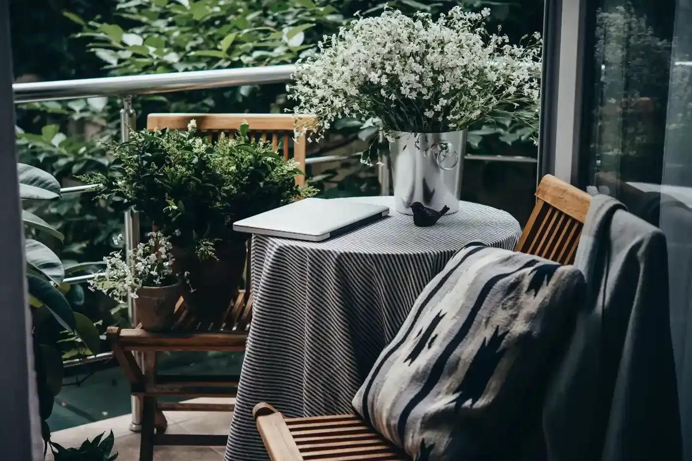 Un acogedor balcón cuenta con dos sillas de madera, una mesa con un mantel estampado.
