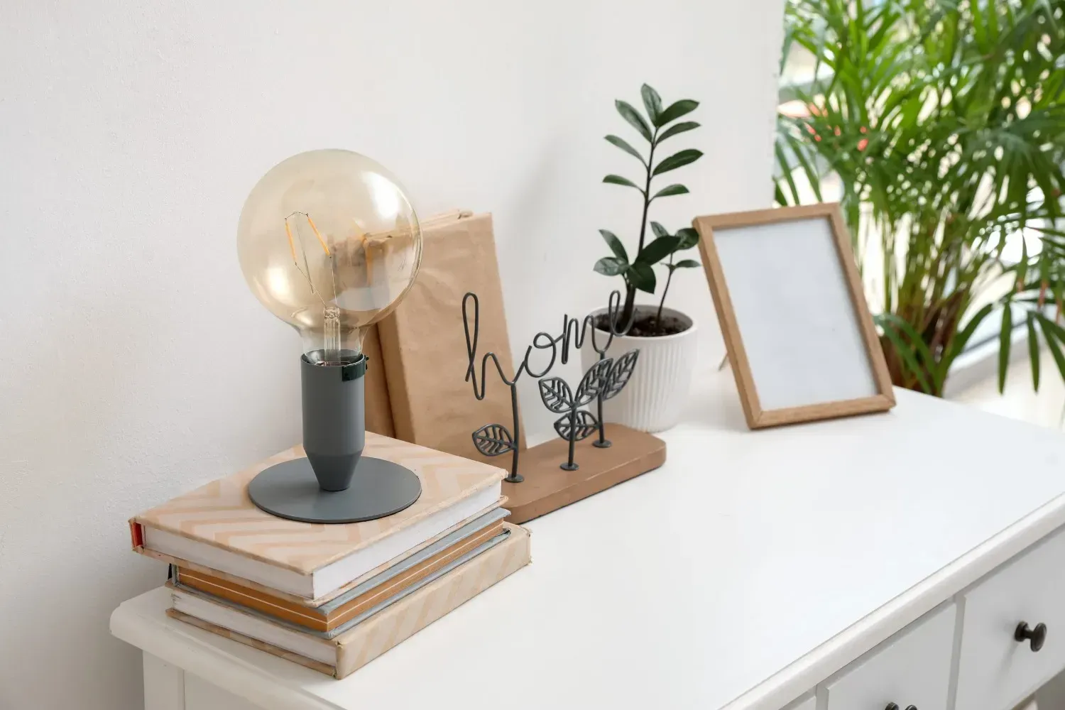 Una lámpara, libros apilados, objetos de decoración para el hogar, una pequeña planta y un marco de fotos.