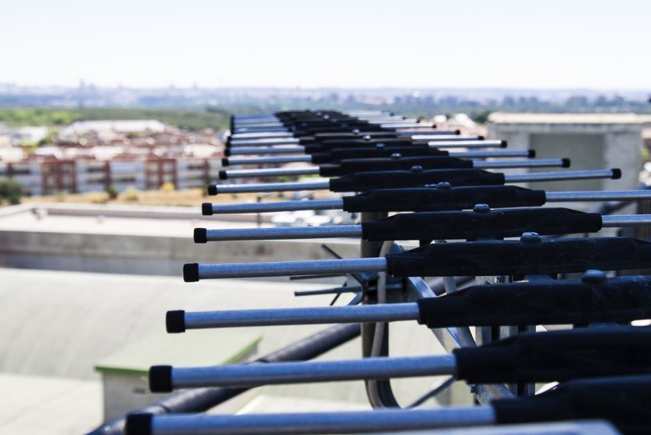 Conjunto de antenas cilíndricas horizontales sobre un tejado, con un paisaje urbano borroso al fondo.
