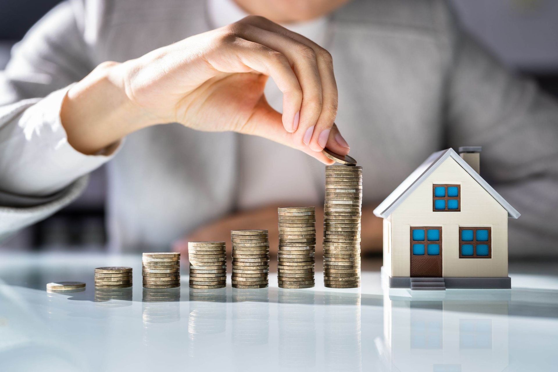 Persona apilando monedas cerca de una casa en miniatura, lo que representa una creciente inversión inmobiliaria.