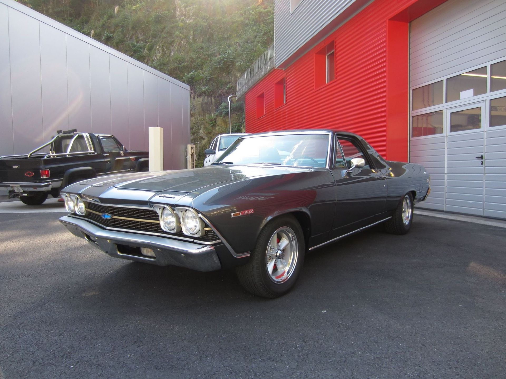 Dunkelgrauer Chevrolet El Camino von 1968, geparkt vor einem roten Gebäude.