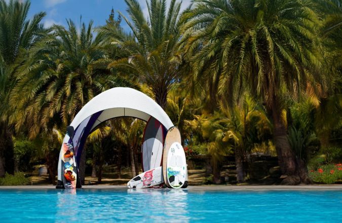 White arch over turquoise pool with paddleboards, backed by lush palm trees