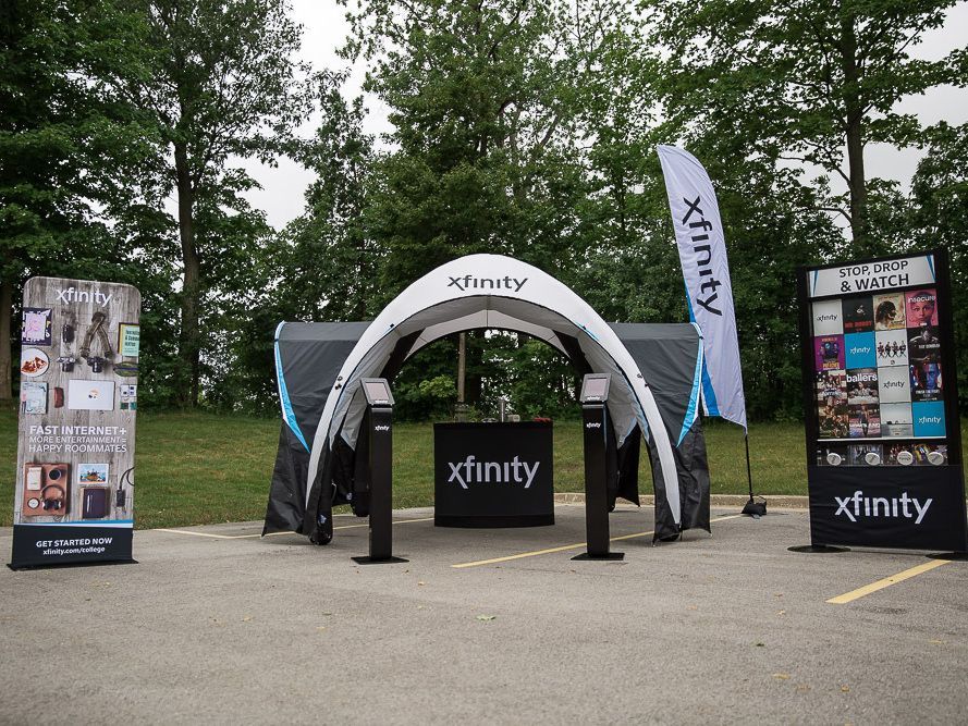 Xfinity outdoor booth with arch, banners, and display panels in a park setting