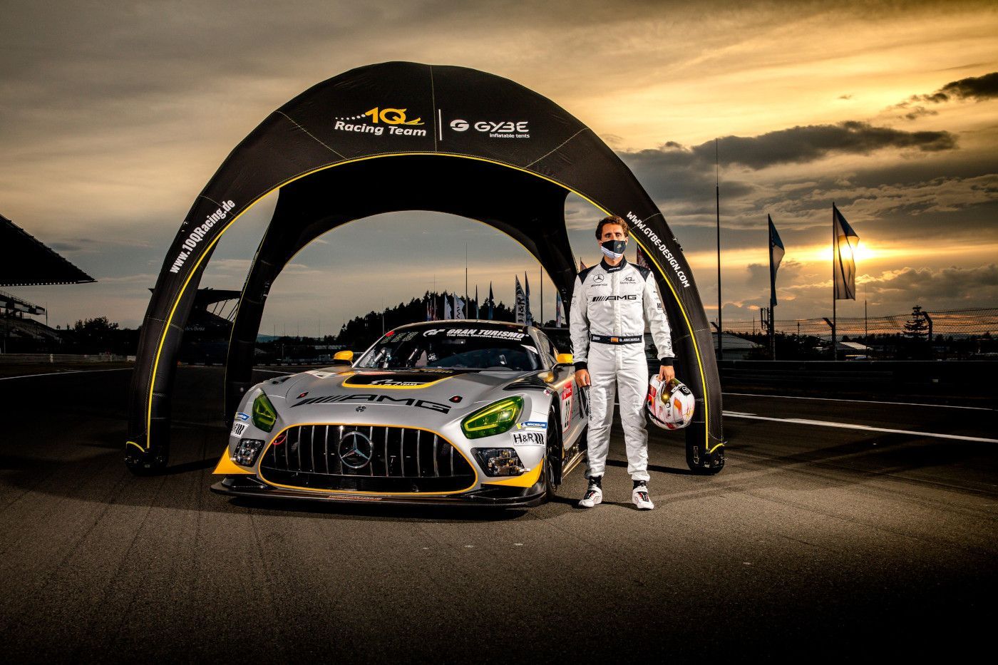 Race car and driver under a black arch at sunset on a track