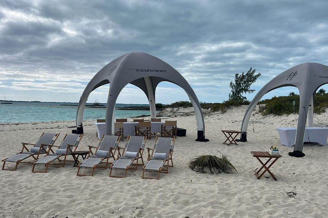Beach lounge chairs under white tents on a cloudy shoreline, with calm ocean in the background.