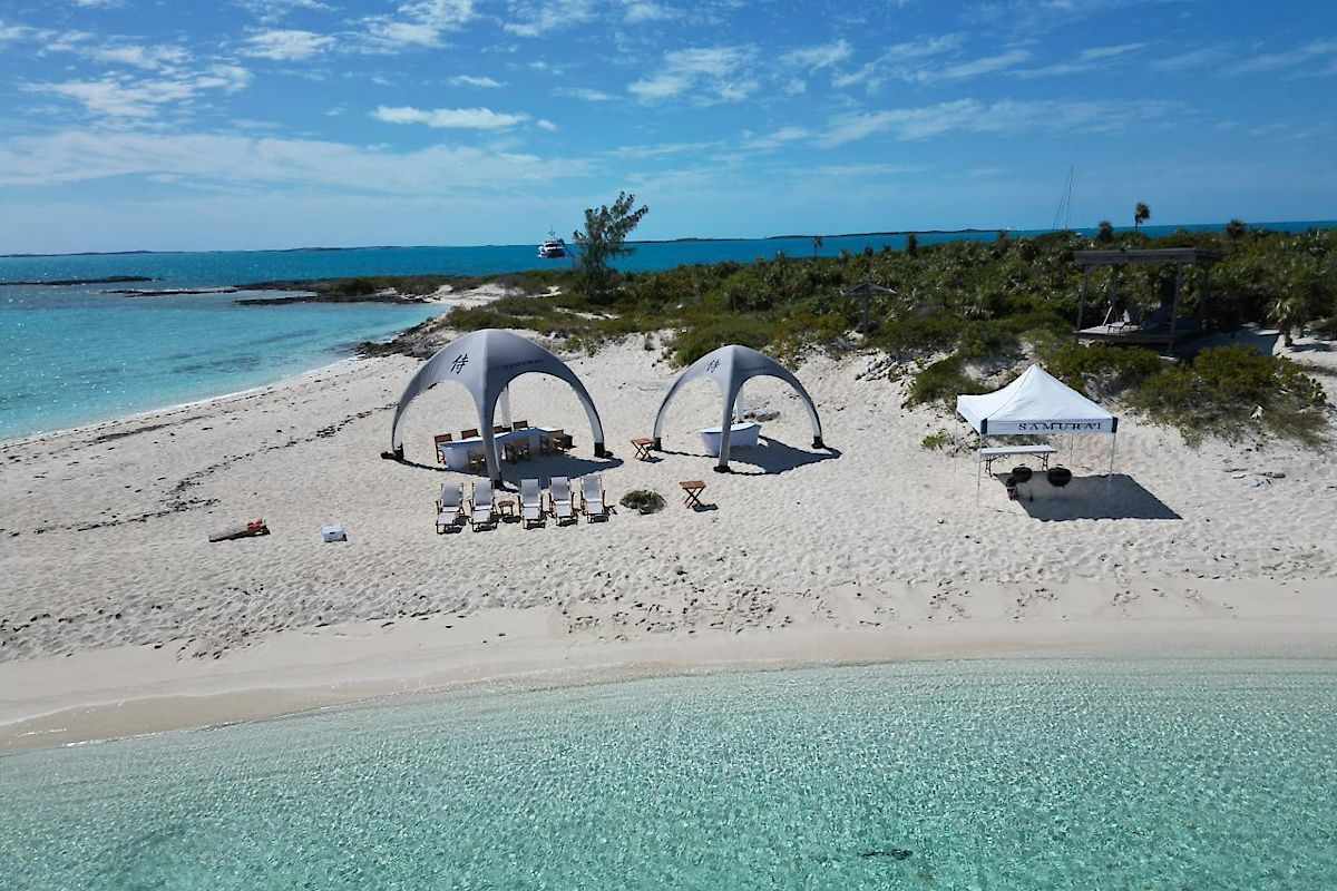 White sandy beach with two dome tents and a lounge area beside turquoise water under a clear blue sky