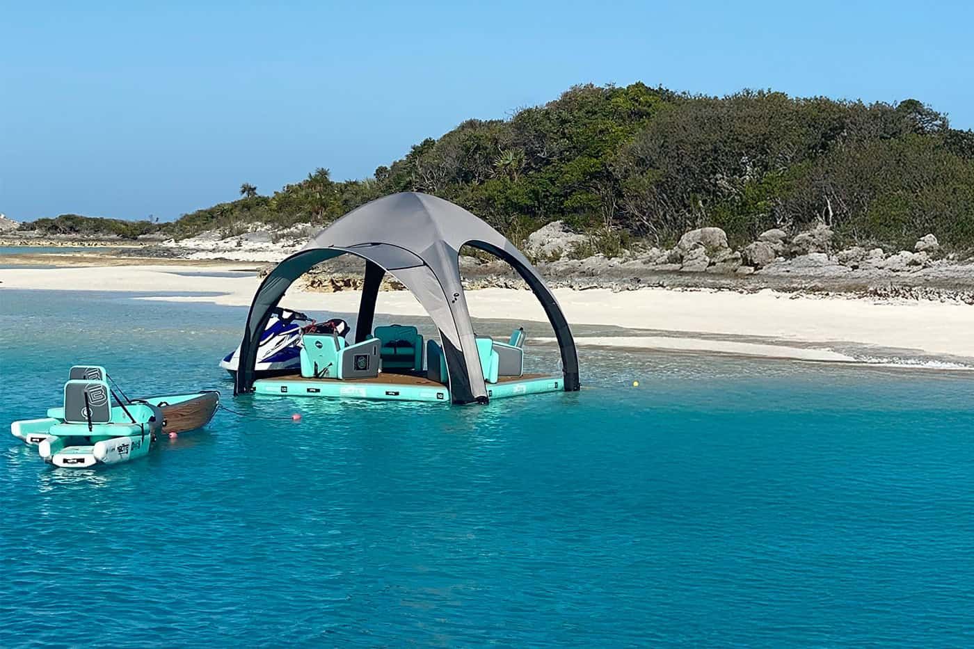A turquoise boat with a canopy floats near a white sandy beach and rocky green island.