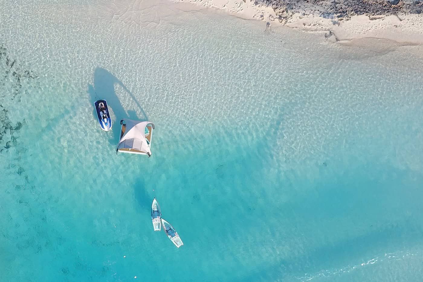 Aerial view of two boats in turquoise water near a pale sandy shore