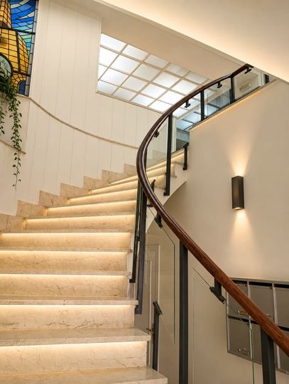 Escalera curva con escalones iluminados y barandilla de cristal en un interior moderno.