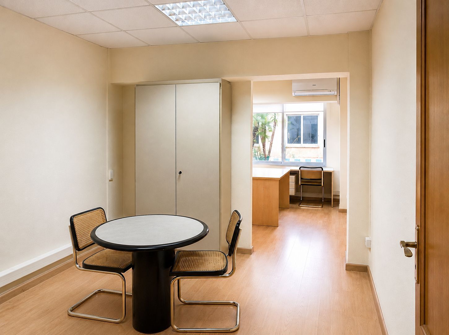 Sala de descanso luminosa con mesa, sillas, armarios y un escritorio junto a una ventana soleada.