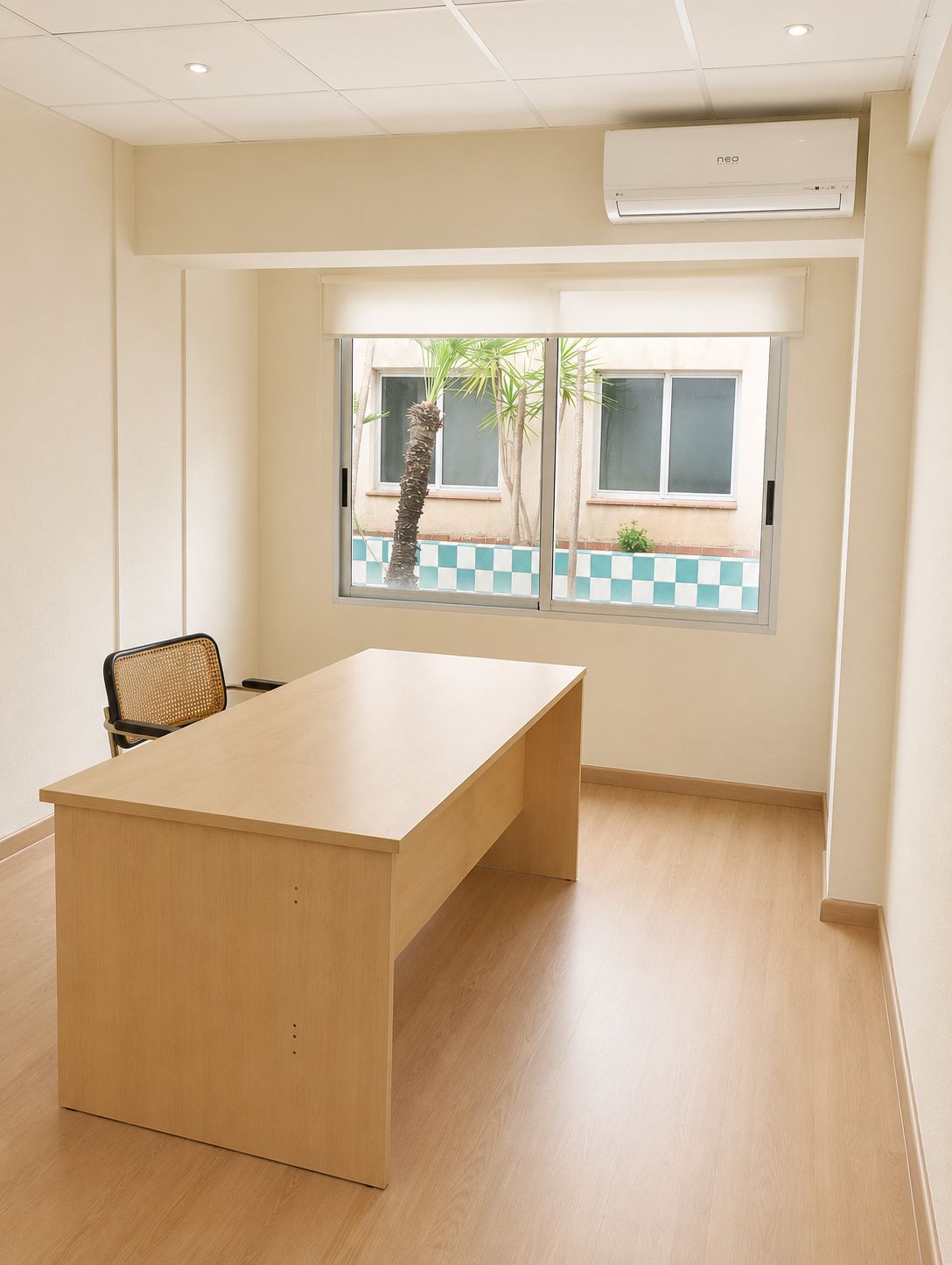 Pequeña oficina con escritorio de madera, ventana, silla y aire acondicionado en una habitación luminosa.