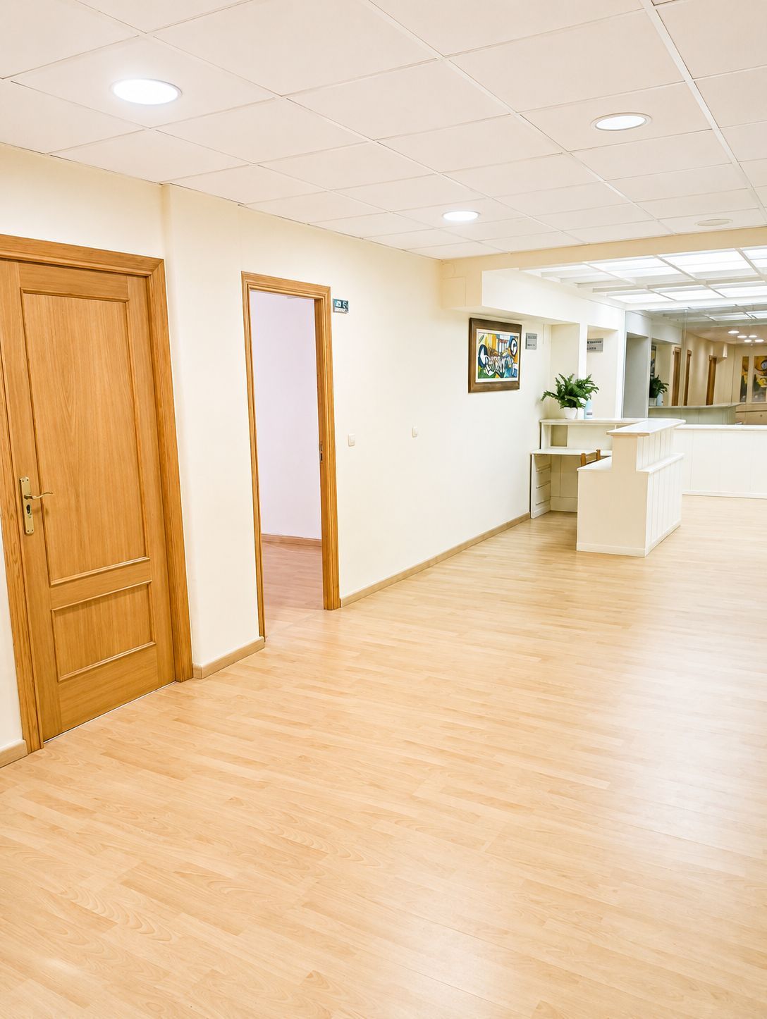 Pasillo vacío con puertas de madera, suelo de madera clara y un mostrador de recepción a lo lejos.