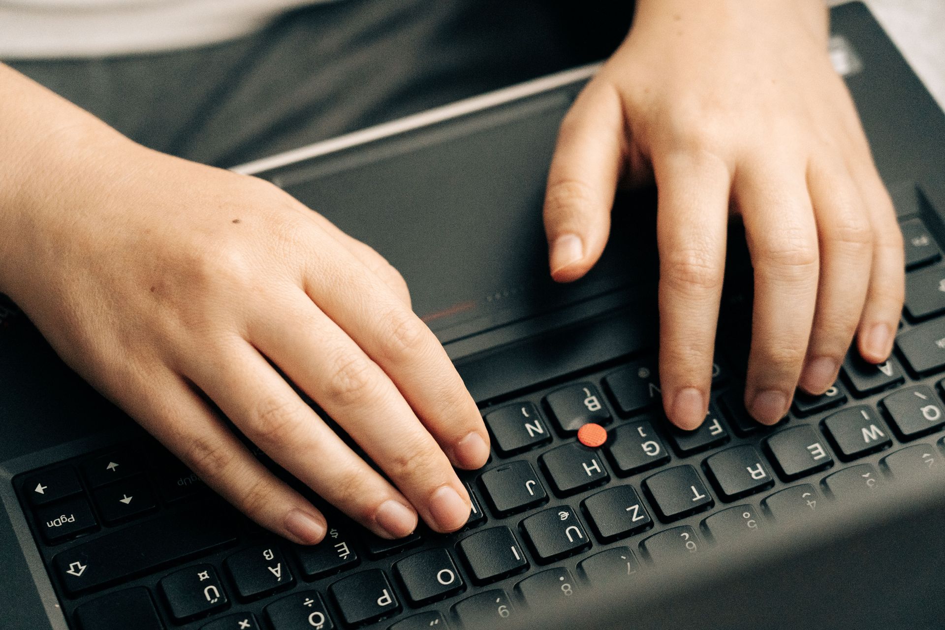 Manos escribiendo en el teclado negro de un portátil con un botón TrackPoint rojo
