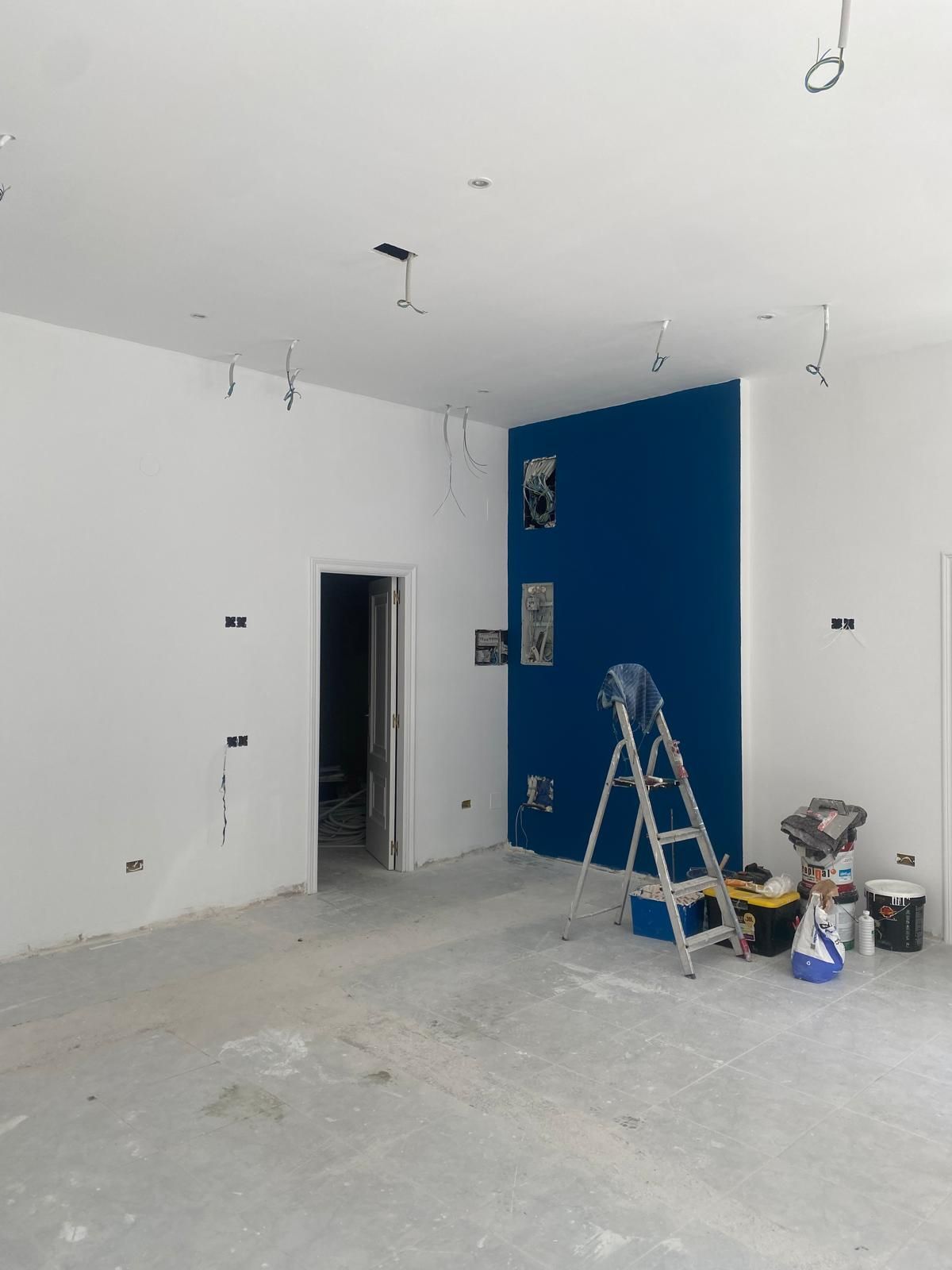 Habitación interior en construcción con paredes blancas, pared decorativa azul, escalera y materiales de pintura.