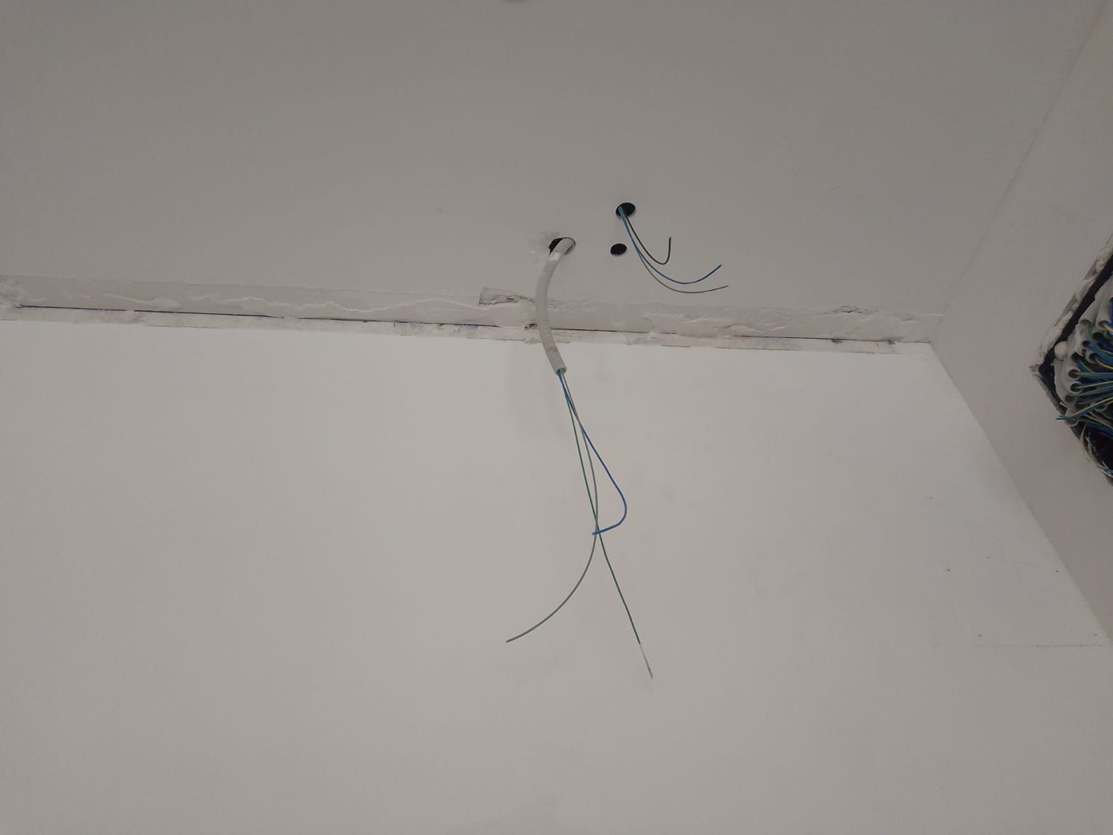 Techo con cables eléctricos expuestos y pared blanca irregular cerca de la esquina.