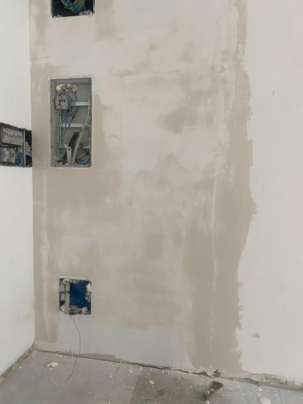 Pared sin terminar con cajas eléctricas expuestas y paneles de yeso irregulares en una habitación en renovación.