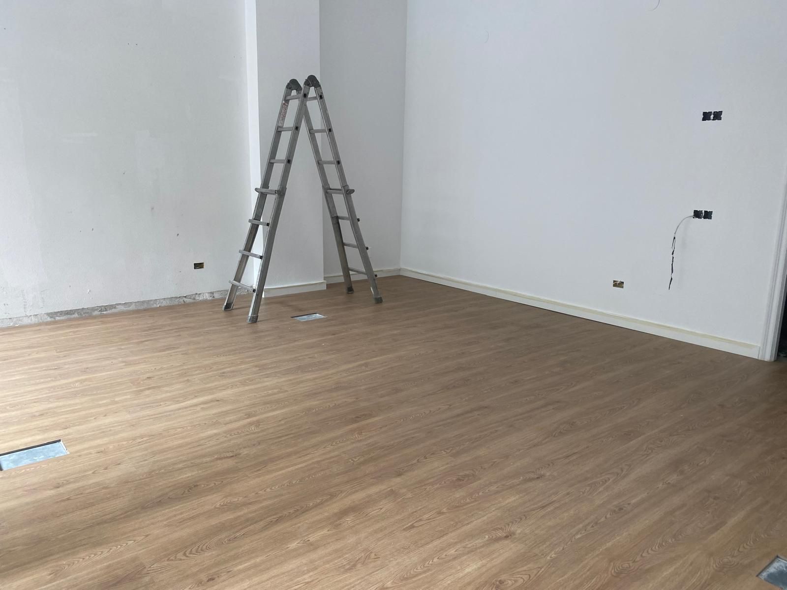 Habitación vacía con suelo de madera, paredes blancas y una escalera colocada en una esquina.