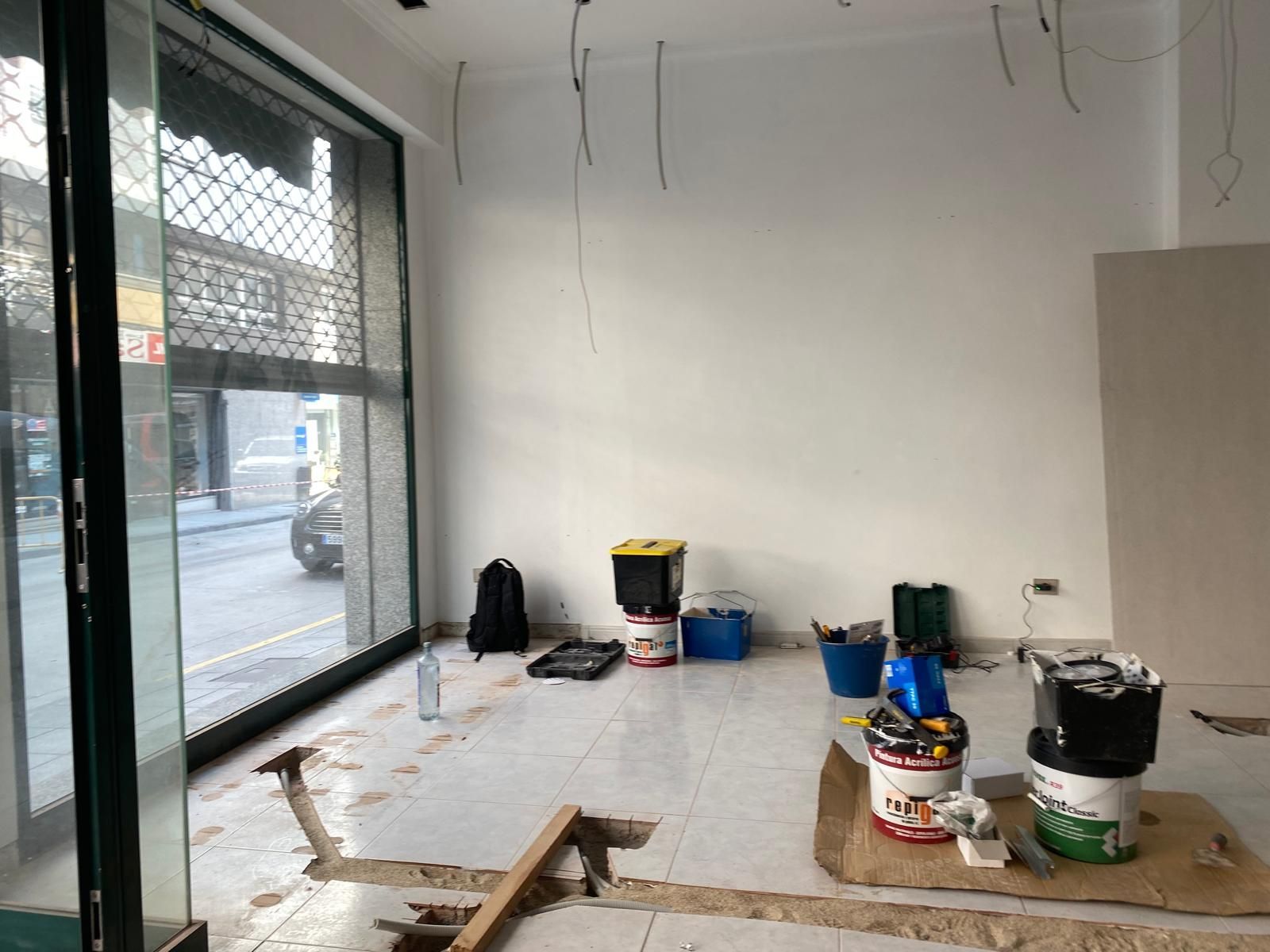 Habitación parcialmente renovada con cubos de pintura, herramientas y una gran ventana que da a la calle.