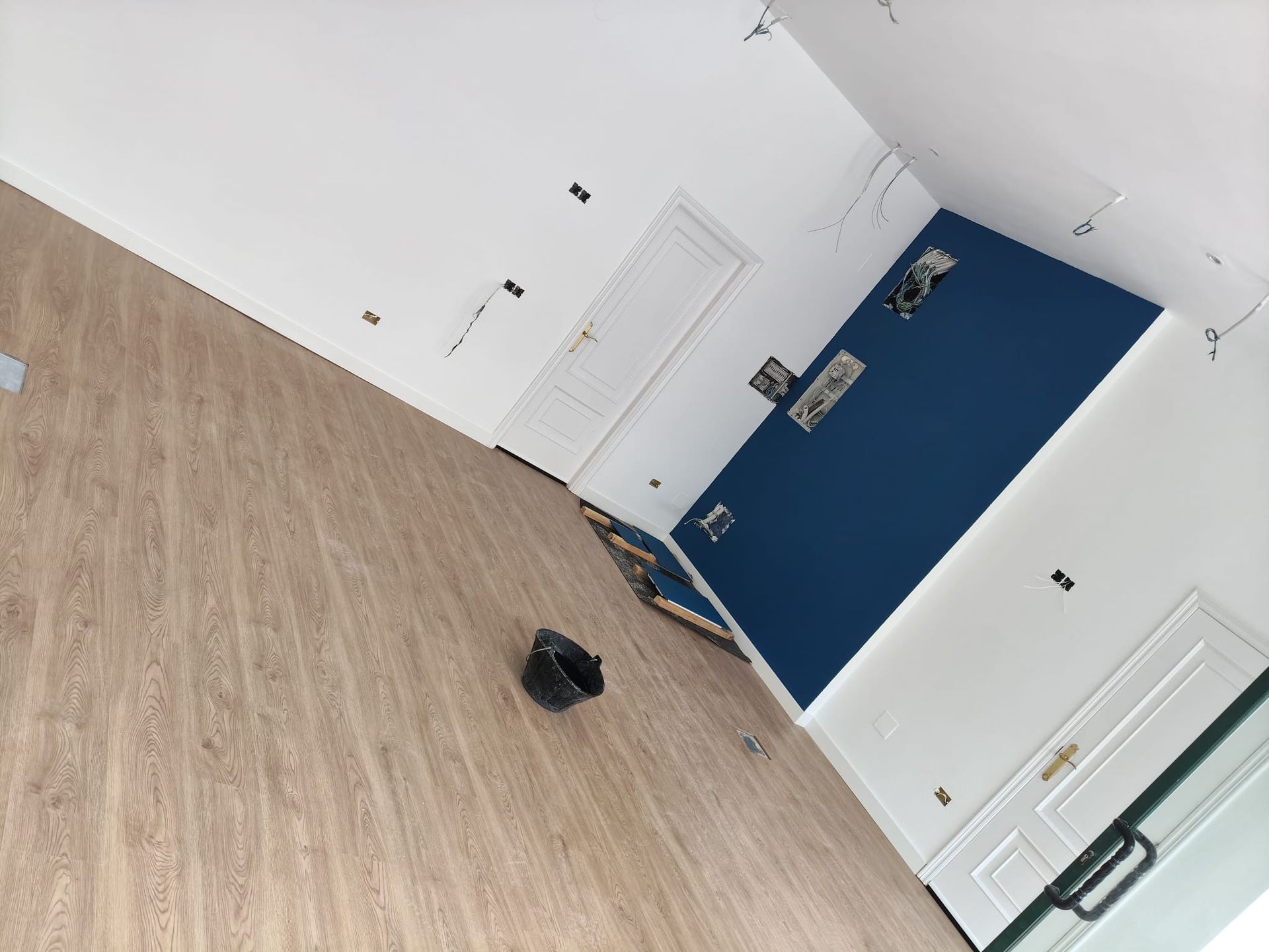 Habitación vacía con suelo de madera, paredes blancas, una pared decorativa azul y una puerta cerrada.