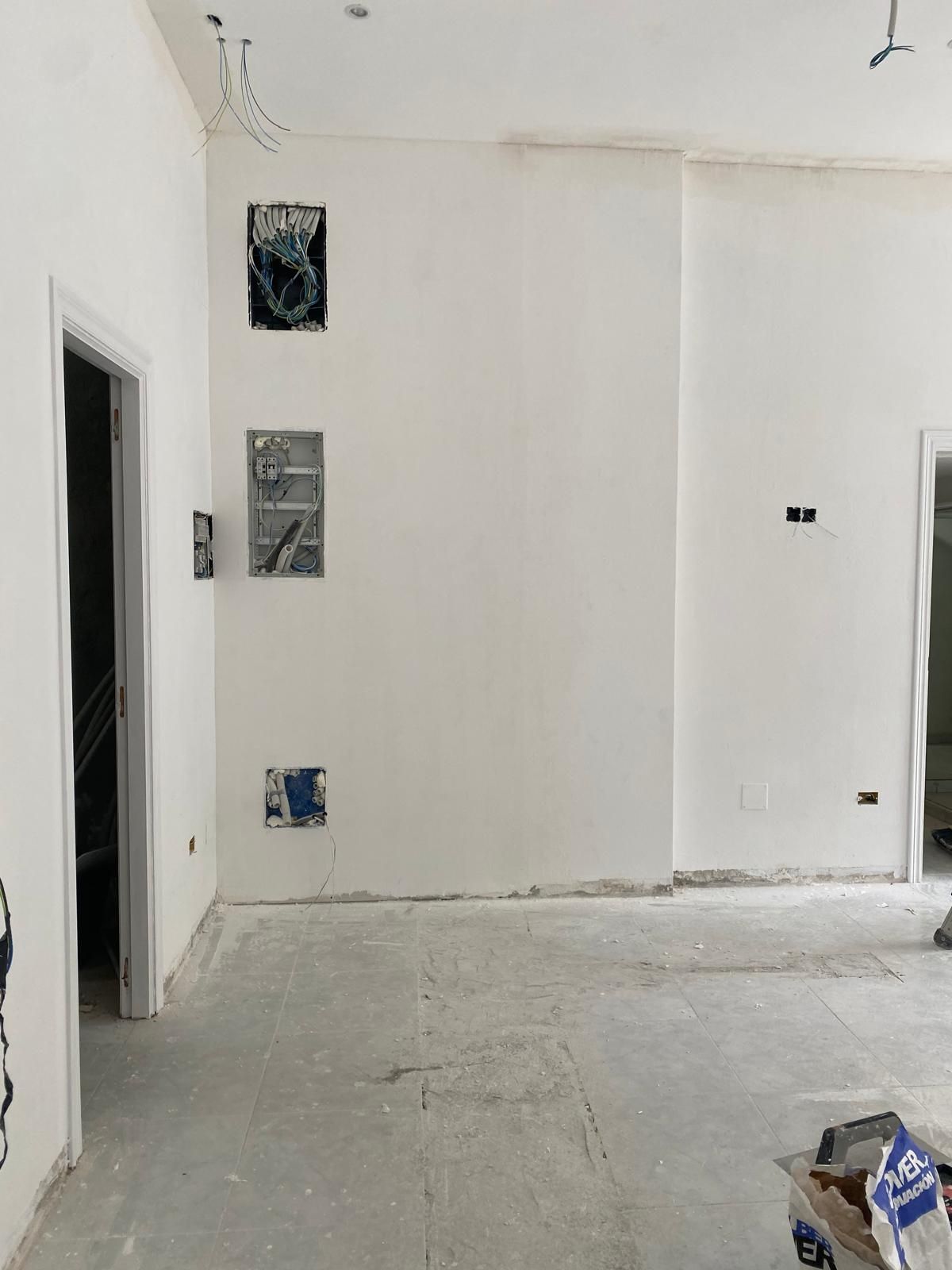 Habitación blanca sin terminar, con paredes desnudas, puertas abiertas y materiales de construcción en el suelo.