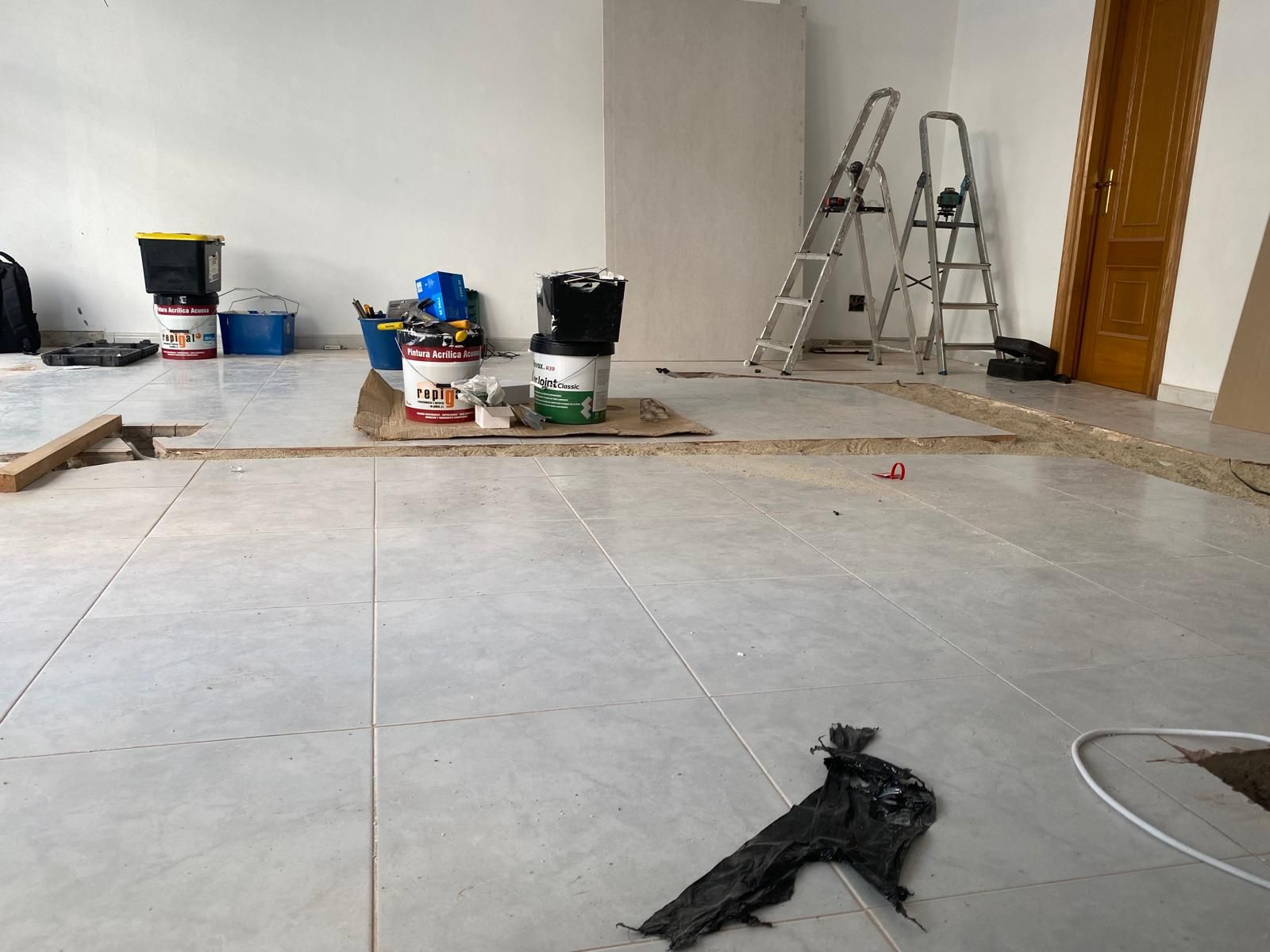 Habitación parcialmente alicatada con escaleras, cubos de pintura y herramientas durante la reforma.