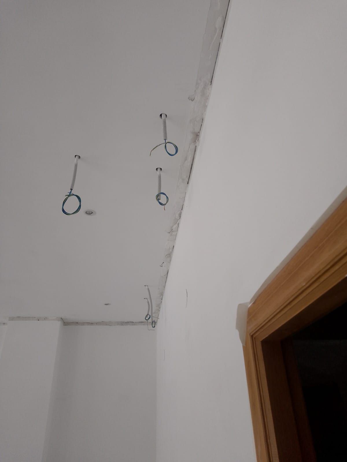 Techo con tres cables eléctricos expuestos colgando cerca de una puerta y bordes de yeso sin terminar.