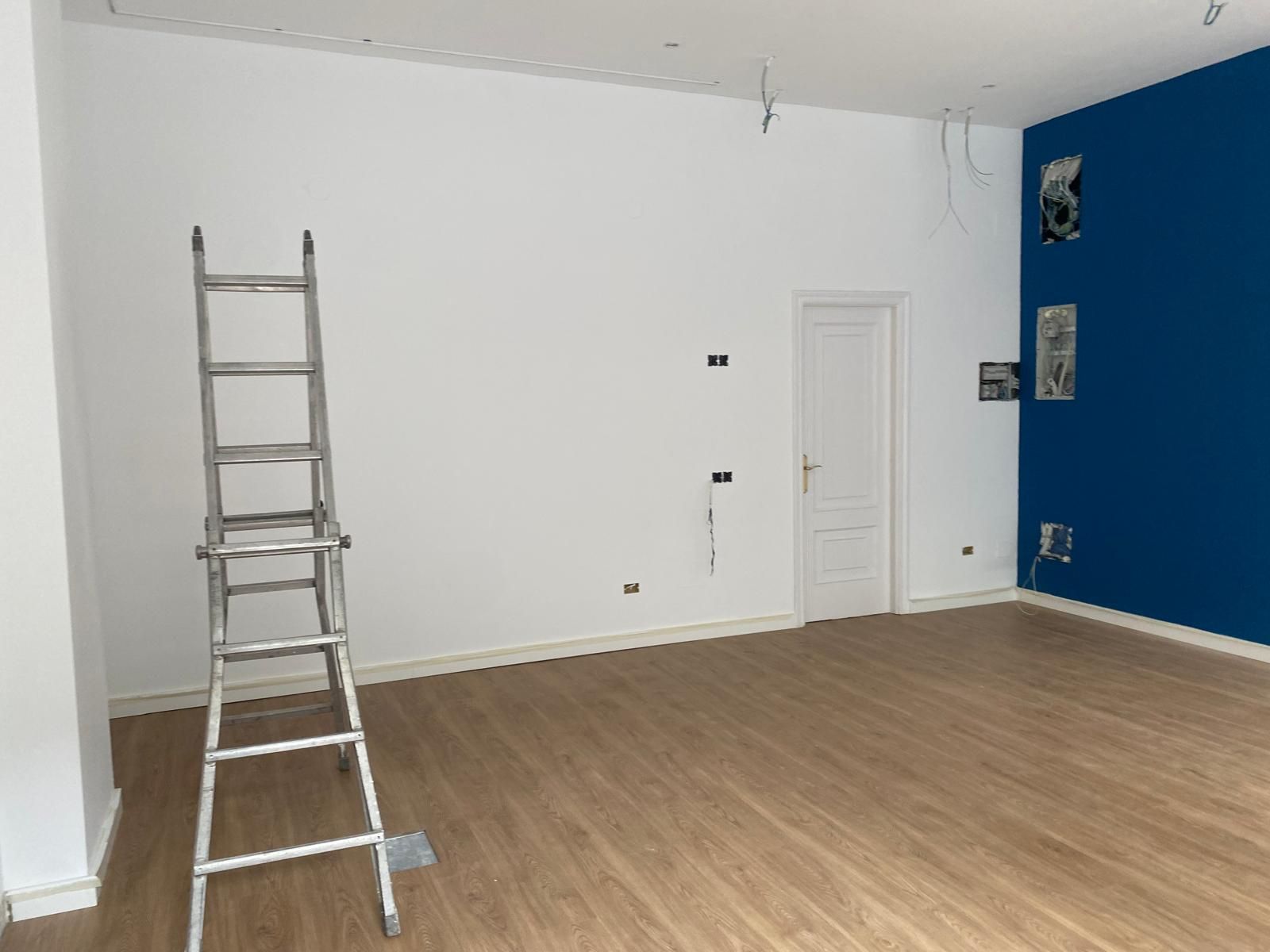 Habitación vacía con paredes blancas, suelo de madera, una pared decorativa azul y una escalera situada cerca del lado izquierdo.