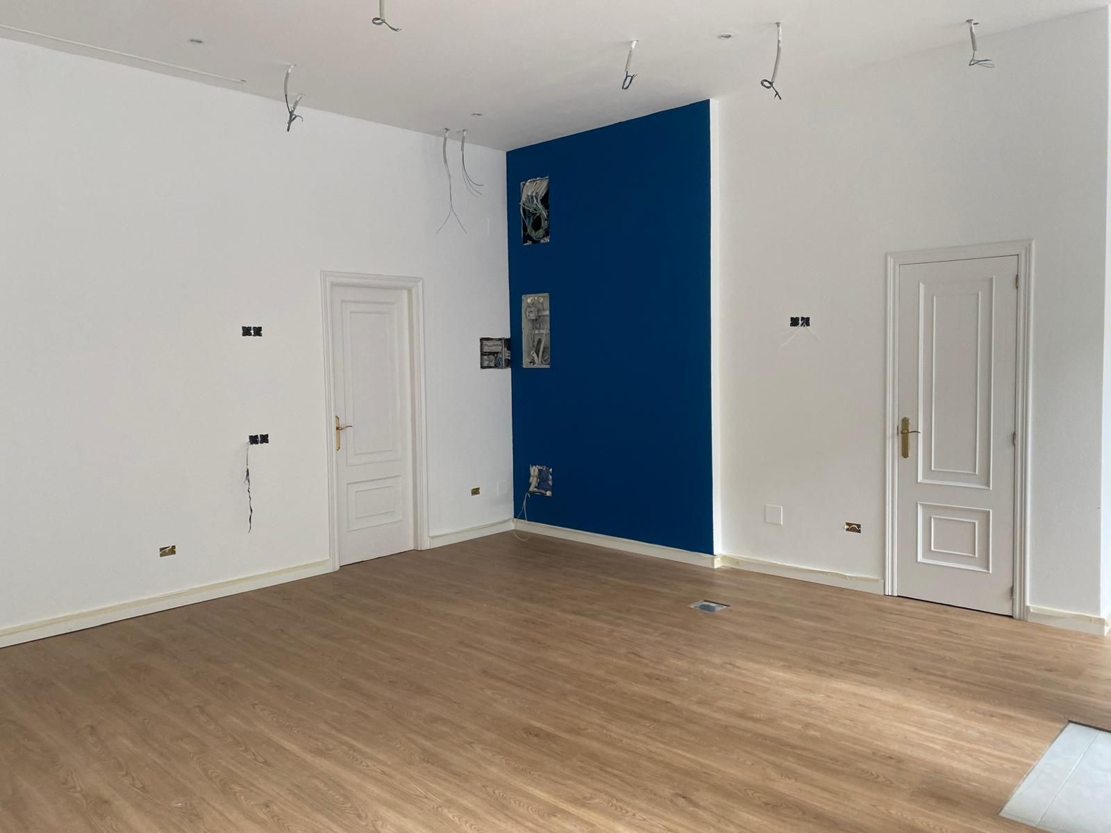 Habitación blanca vacía con suelo de madera, pared decorativa azul y dos puertas blancas.