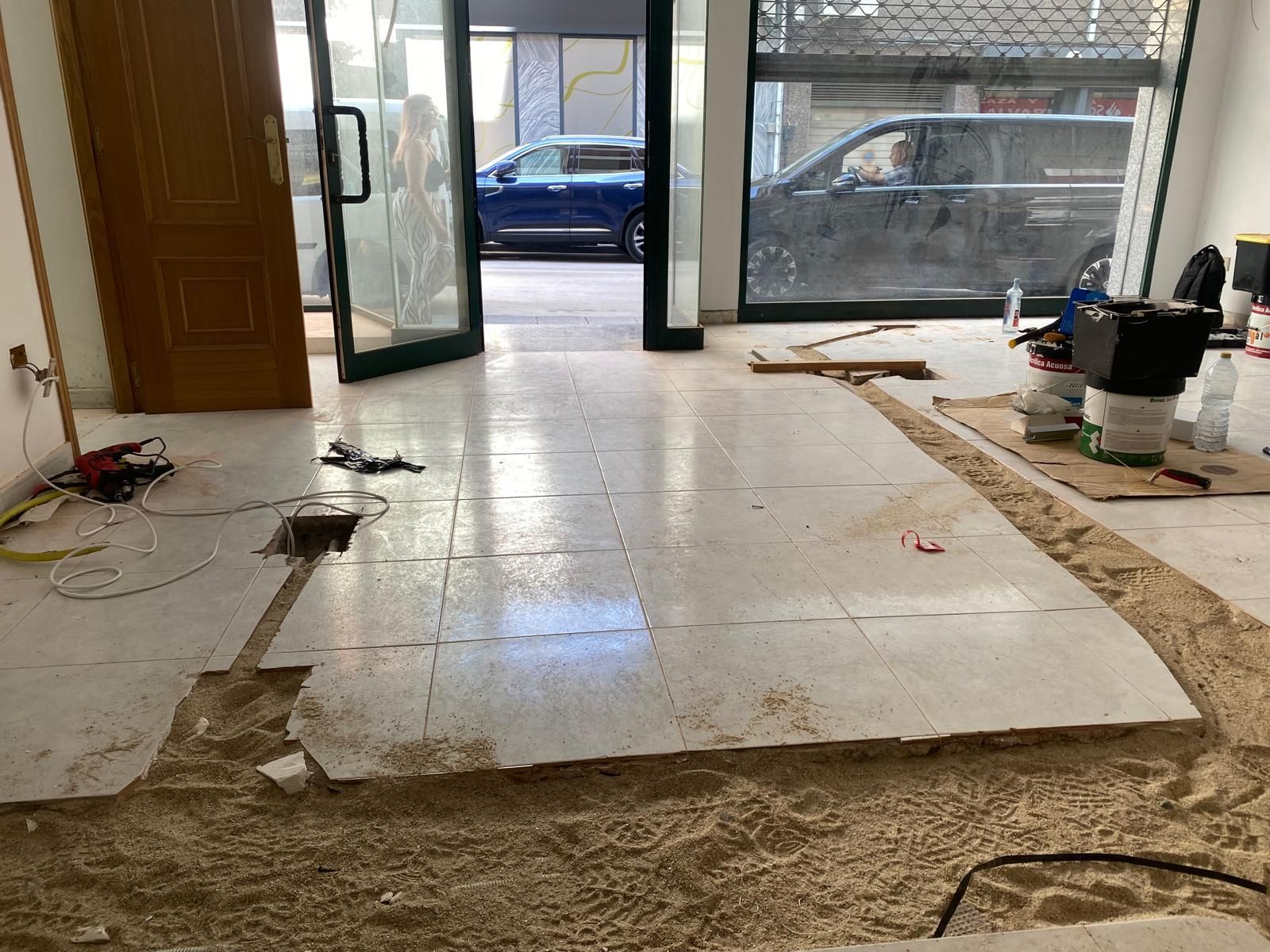 Habitación parcialmente renovada con suelo de baldosas, puertas de cristal abiertas y herramientas de construcción cerca de las paredes.