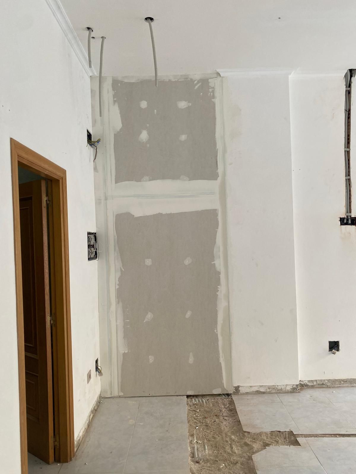Habitación interior en obras, con parches de pladur sin terminar y cables del techo a la vista.